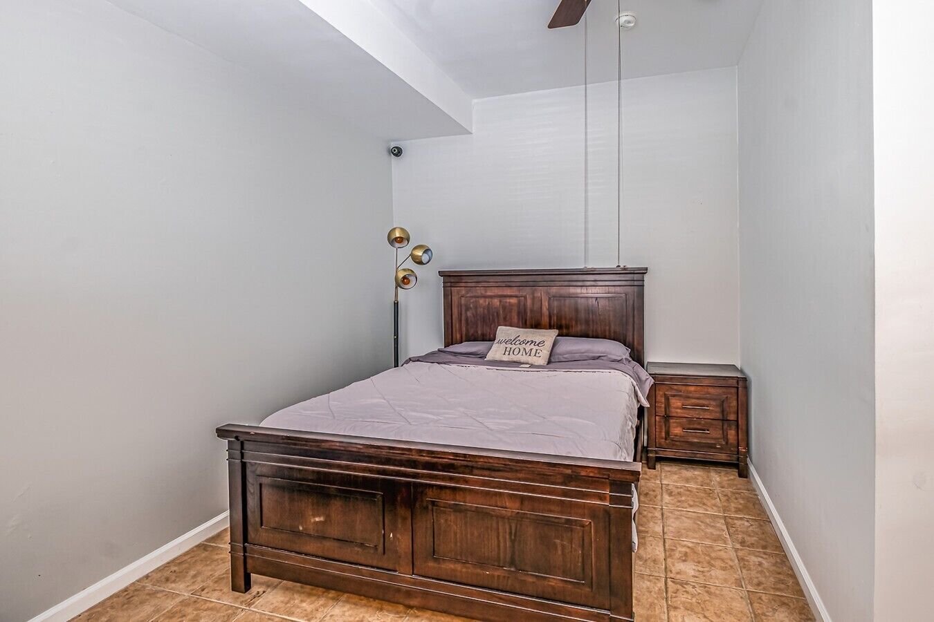 A bedroom with a wooden bed, a nightstand, a floor lamp, and a ceiling fan.