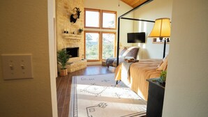 A bedroom with a bed, a TV, a lamp, a fireplace, and a stone wall. - The Ranch House (Hondo)