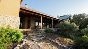 A house with a stone exterior, a covered porch with chairs, and a stone staircase leading to the entrance. - The Ranch House (Hondo)