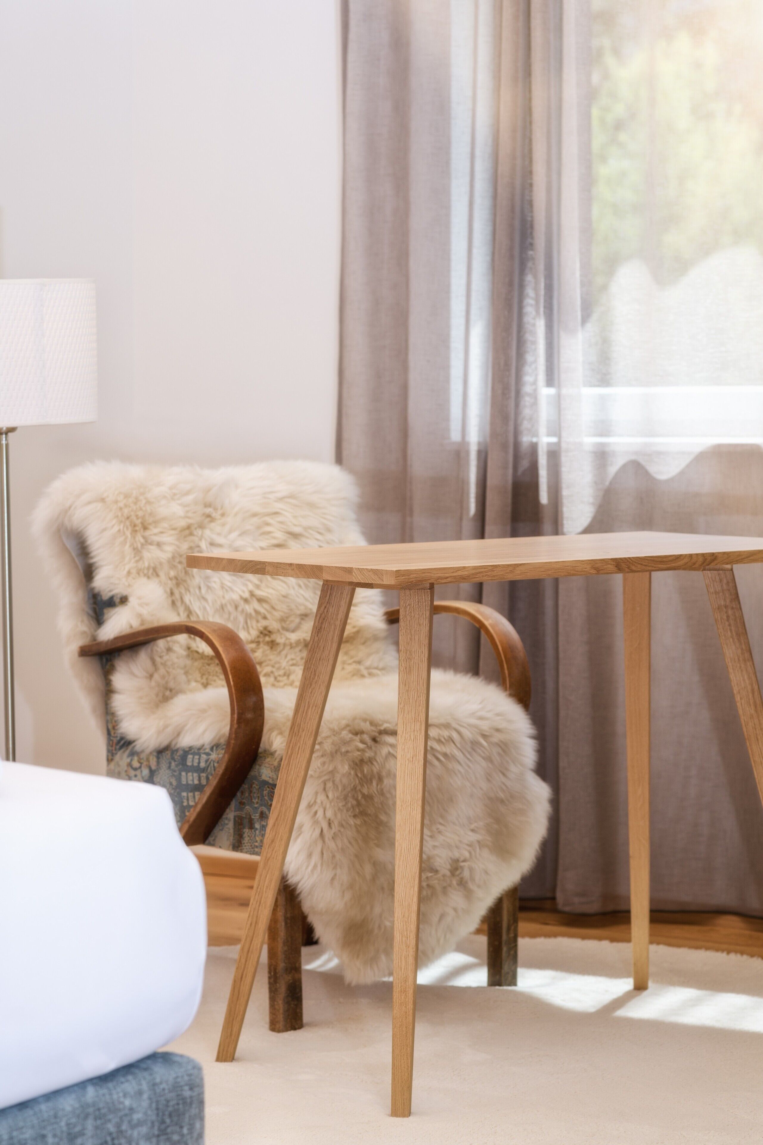 A room with a wooden table, a fur-covered chair, and a lamp.