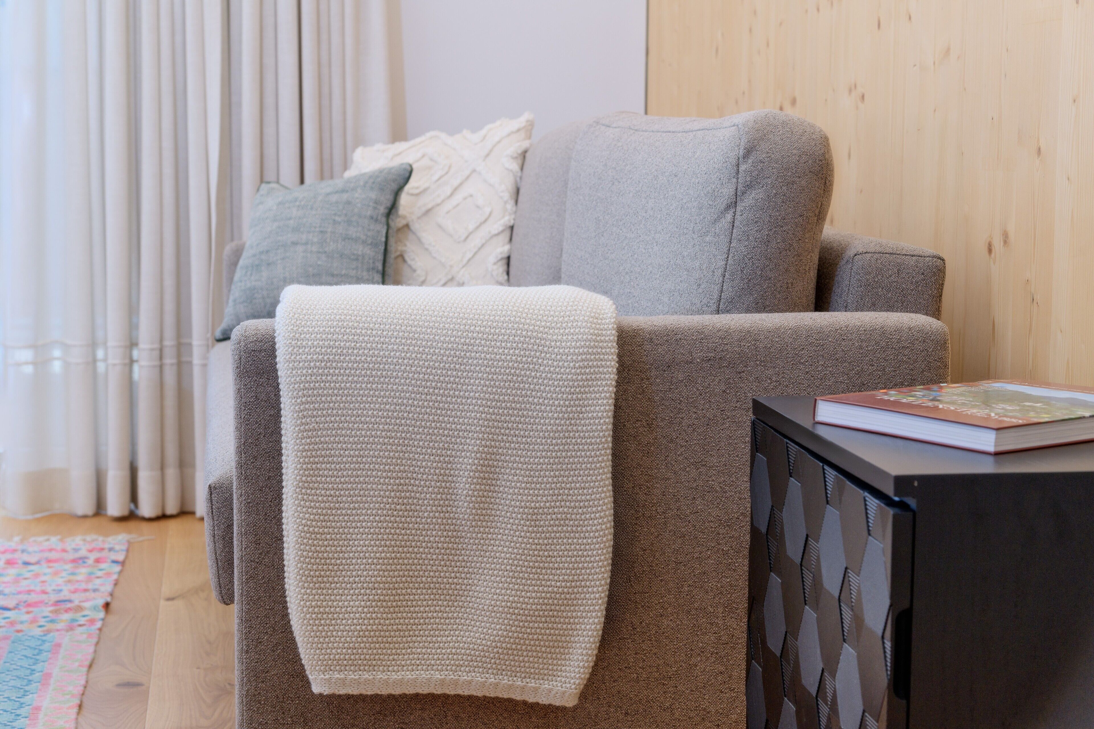 Una sala de estar con un sofá, un plaid y un libro sobre una mesita.