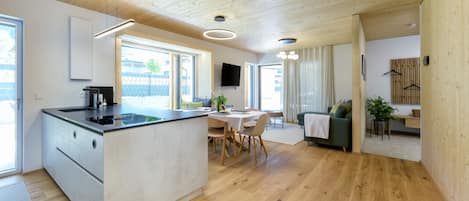 A modern kitchen with a central island, dining area with a table and chairs, a sofa, and a TV mounted on the wall.