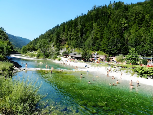 A river with clear water, surrounded by greenery and a forested hillside.
