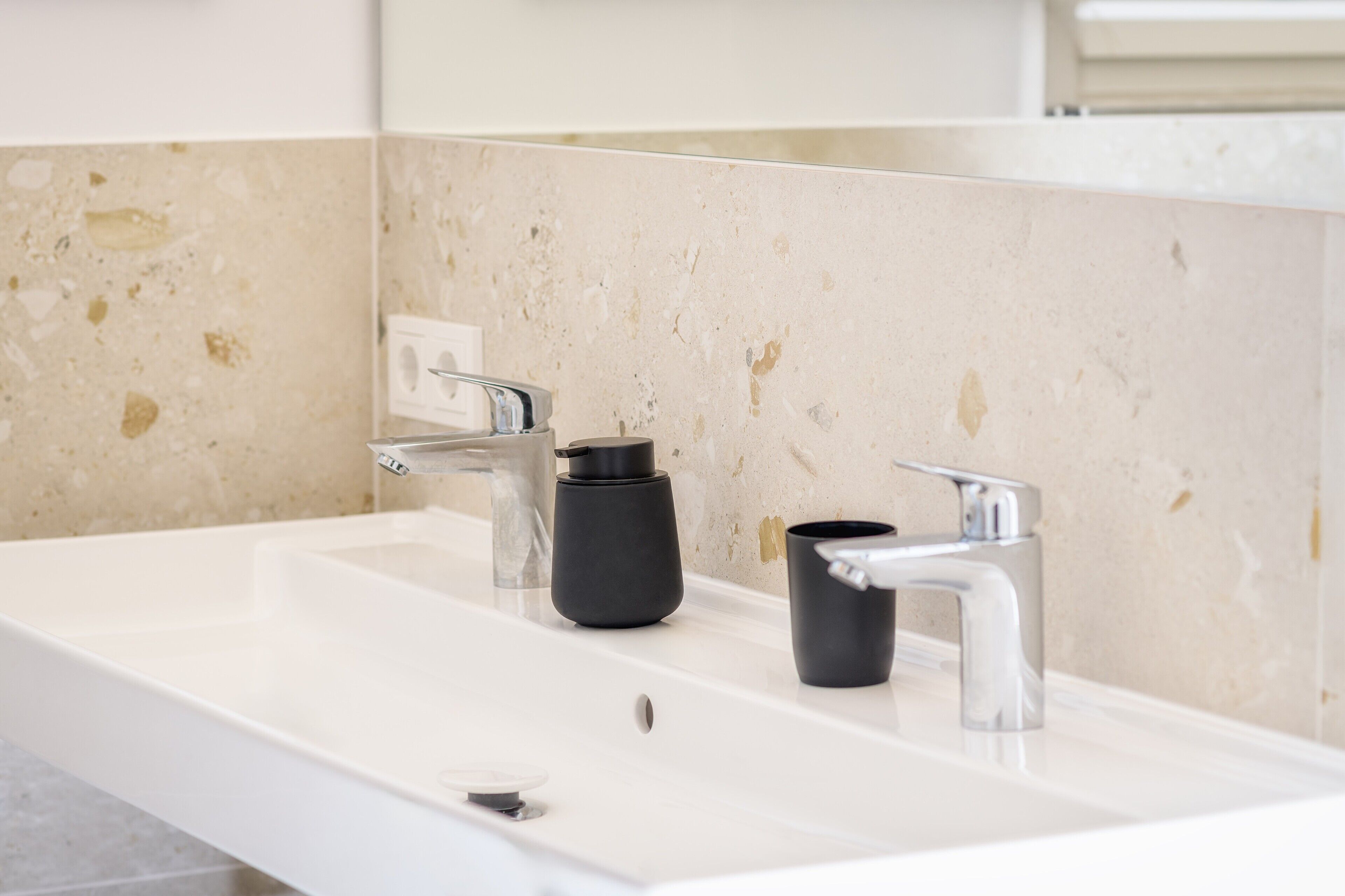 Un baño con lavamanos blanco, dos grifos y un espejo.
