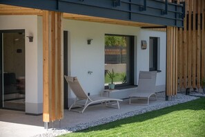 Un espacio lounge exterior moderno con dos sillones, una mesita y una planta en maceta.