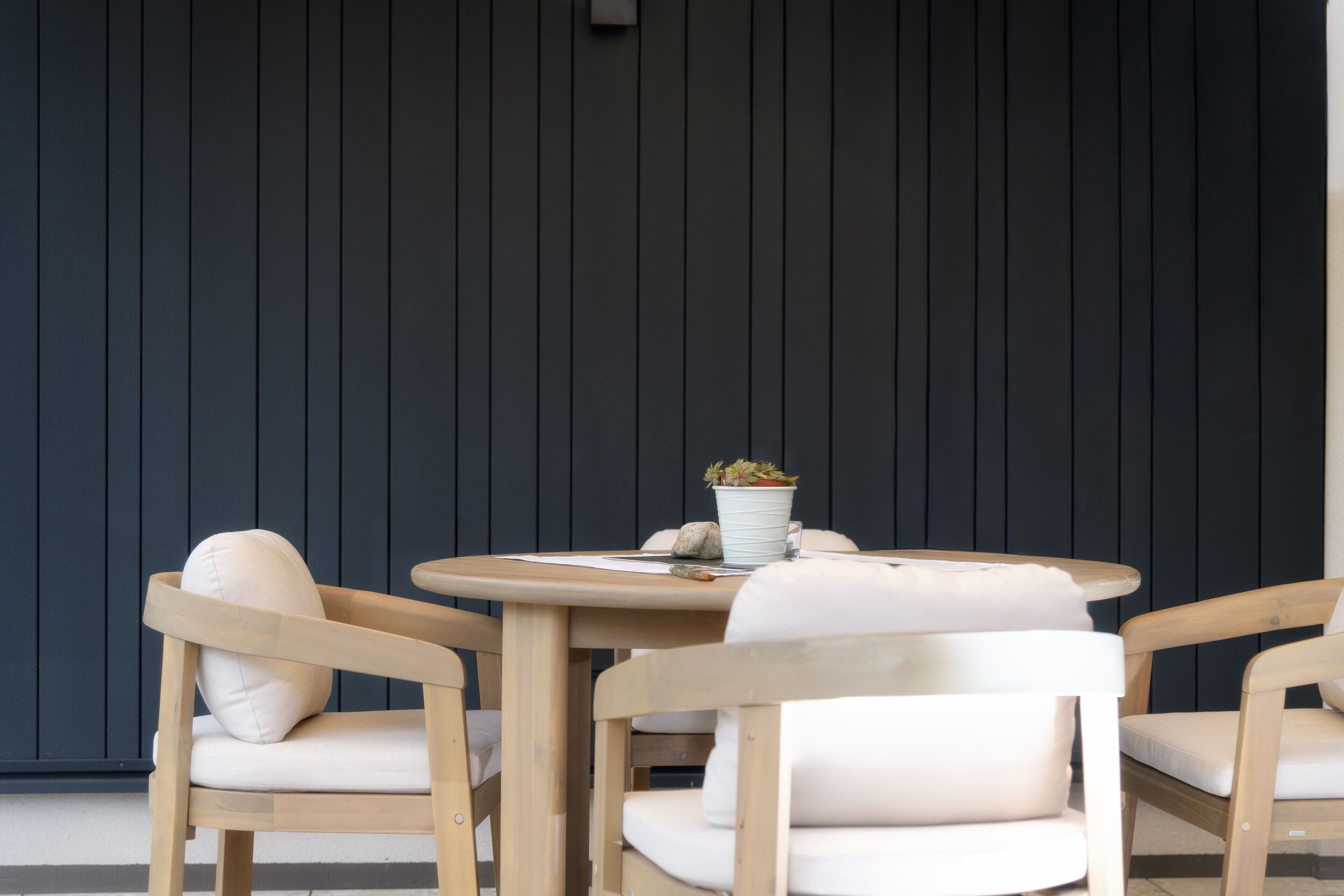 A round wooden table with two chairs, a potted plant, and a glass of water.
