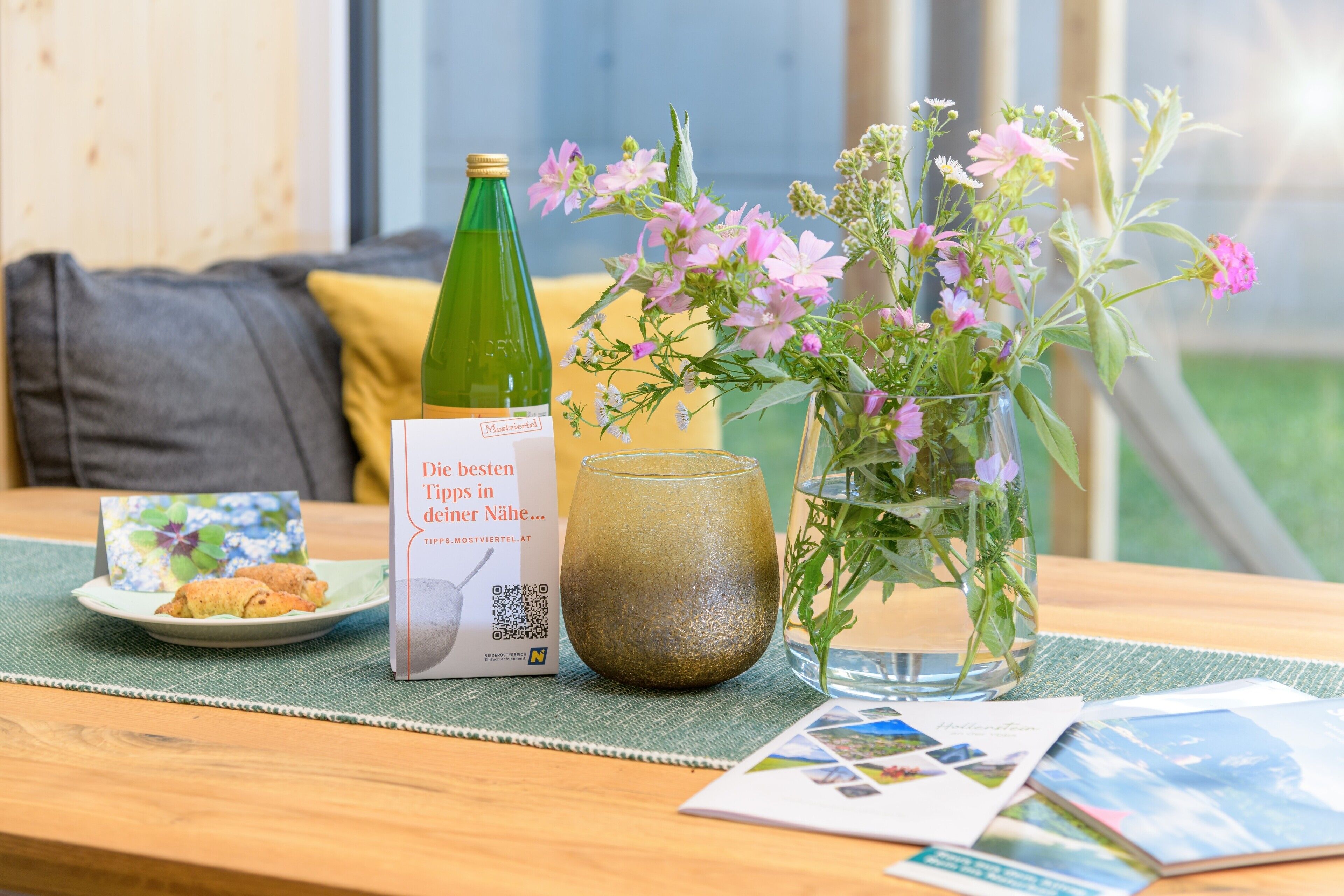 Een tafel met een fles, een glas, een bord eten, een boekje en een vaas met bloemen.