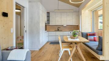 A modern kitchen with wooden cabinetry, a dining table with chairs, a built-in bench with cushions, and a view through a large window.
