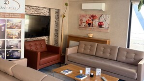 Una sala de estar moderna con sofá, sillón y mesa de centro. Hay un televisor, una pared de piedra y un cuadro en la pared.