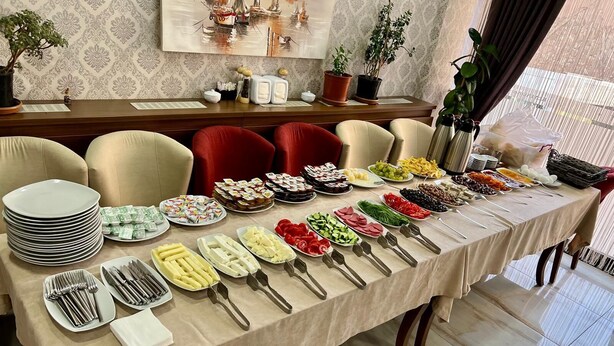 Una mesa de buffet con diversos alimentos y utensilios, rodeada de sillas y un papel tapiz estampado.