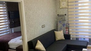 Una sala moderna con un sofá seccional, una mesita blanca y una cama con una colcha roja.