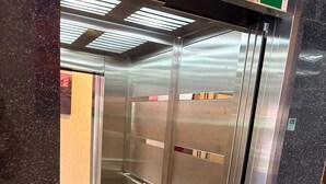 Interior de un ascensor con paredes metálicas, una pantalla digital y un piso indicado por una flecha direccional.