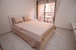 A bedroom with a bed, a bedside table, a mirror, and a view of an outdoor patio.