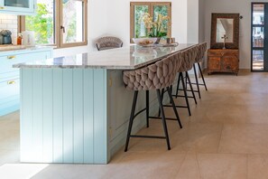 A kitchen with a central island, bar stools, a wooden cabinet, and a view through the window.