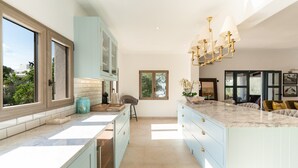 A modern kitchen with light blue cabinets, a marble countertop, and a chandelier. - Exclusive Mediterranean Villa with Private Pool in Cala d'Or (Santanyí)