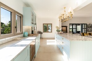 A modern kitchen with light blue cabinets, a marble countertop, and a chandelier.
