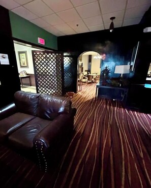 A room with a brown leather sofa, a patterned carpet, a dining area with chairs and a table, and a wall with a decorative panel.