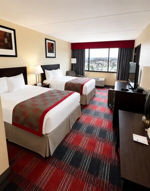 A hotel room with two beds, a desk, a TV, and a large window with a view.