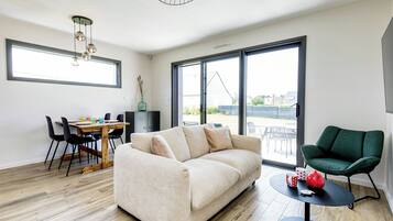 Un salon moderne comprenant un canapé, une table à manger, des chaises, un fauteuil vert et une petite table sur laquelle se trouvent une théière et des tasses.