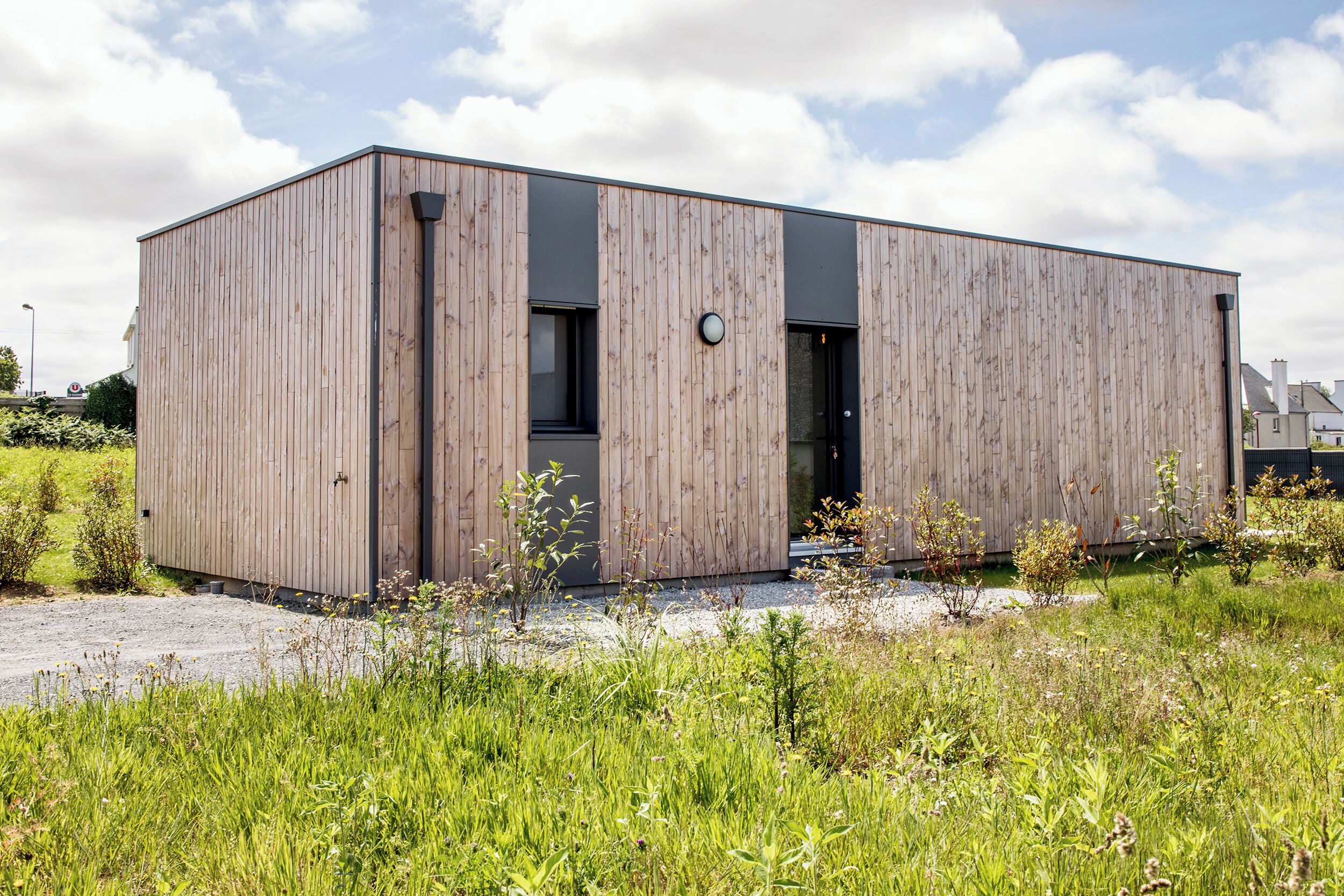 Un bâtiment moderne en bois, doté d’un toit plat, de grandes fenêtres et d’une porte.
