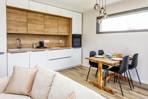 A modern kitchen with wooden cabinets, a dining table with chairs, and a large window. - TI KAZ BREIZH, a new wooden house (Cléder)
