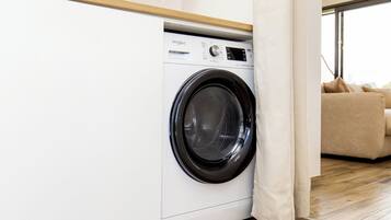 Une buanderie moderne avec un lave-linge Whirlpool à chargement frontal, un plancher en bois et un canapé beige en arrière-plan.