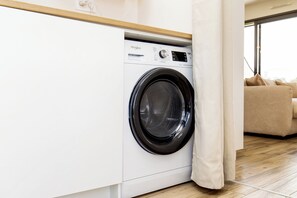 Une buanderie moderne avec un lave-linge Whirlpool à chargement frontal, un plancher en bois et un canapé beige en arrière-plan.