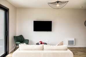 Un salon moderne comprenant un canapé, un fauteuil vert, un téléviseur à écran plat, une petite table agrémentée d’objets décoratifs et une fenêtre offrant une vue agréable.