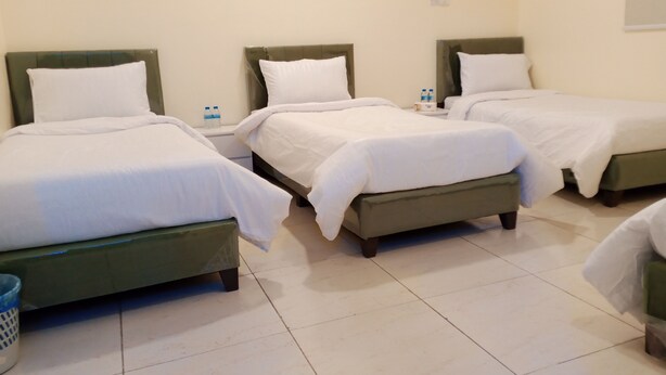 Ein Hotelzimmer mit drei Betten, Fliesenboden und einer Wand-Klimaanlage.