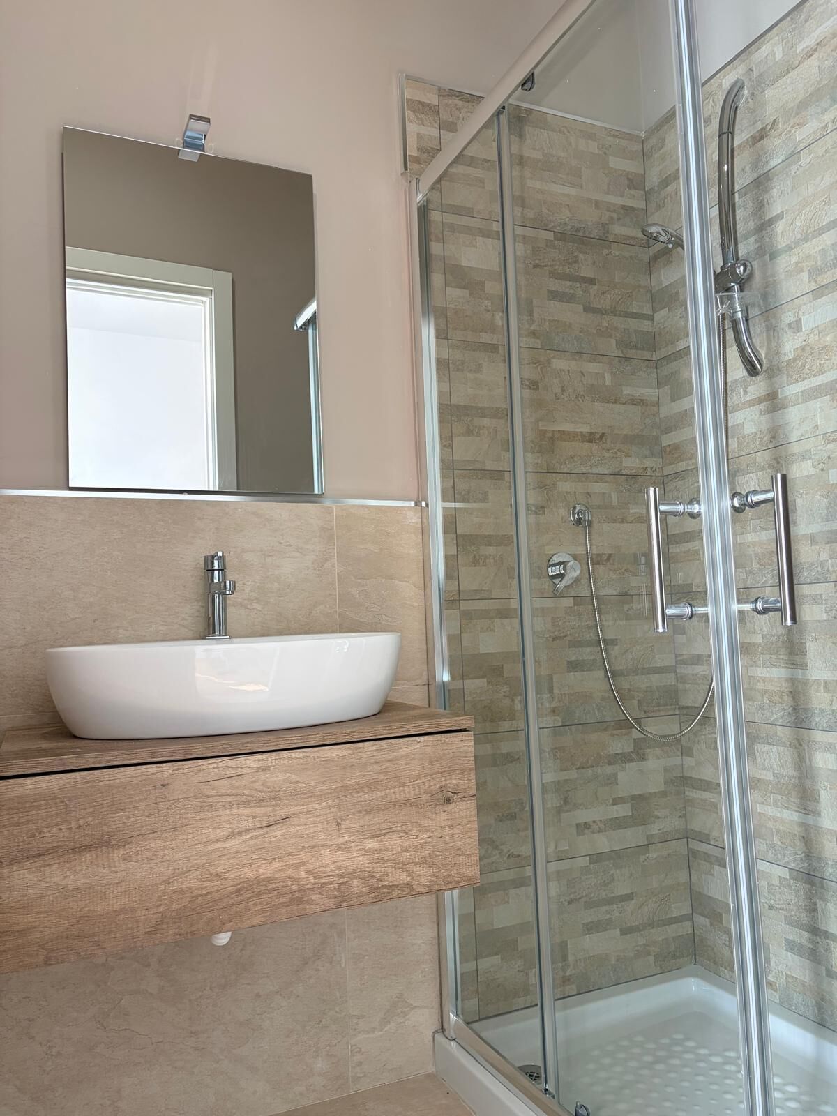 A bathroom with a glass-enclosed shower, a white vessel sink, and a mirror above the sink.