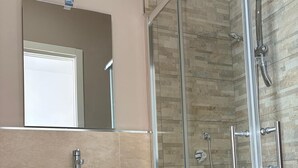Un baño con ducha de vidrio, un lavabo tipo cuenco blanco y un espejo sobre el lavabo.