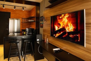 Una cocina moderna con una televisión grande mostrando un fuego, taburetes de bar y una cafetera.