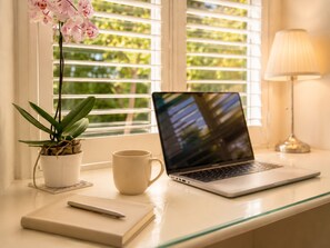 Ein Laptop auf einem Fensterbrett, zusammen mit einem Blumentopf, einer Tasse und einem Notizbuch.