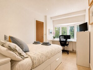 Ein Schlafzimmer mit Bett, Schreibtisch, Stuhl, Fernseher und einem Fenster mit Jalousien.