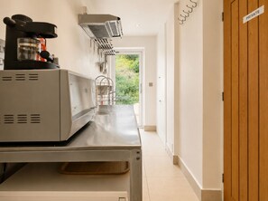 Eine Küchenzeile mit Kaffeemaschine, Wasserspender und kleinem Kühlschrank. Eine Holztür mit dem Schild 'PRIVATE' und Blick ins Grüne.