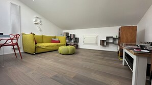 A modern loft apartment with a sloped ceiling, a yellow sofa, a red chair, a wooden dining table, and a built-in bookshelf. - The Loft – Designer Apartment in Castel San Pietro Terme (Castel San Pietro Terme)