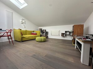 Ein modernes Loft-Apartment mit geneigter Decke, einem gelben Sofa, einem roten Sessel, einem Holzesstisch und einer eingebauten Bücherreol.
