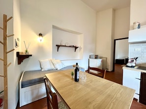 A compact living space with a dining table, a sofa, a small kitchen area, and a built-in shelf.