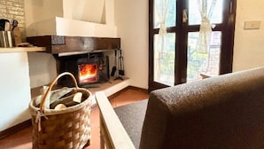 Ein gemütliches Wohnzimmer mit Kamin, einer Bank, einem gewebten Korb und Blick durch eine Glastür.