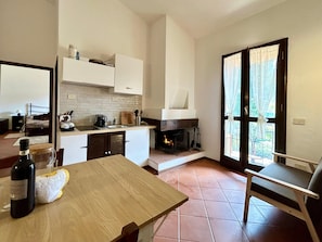 A compact kitchen with a fireplace, a dining table, and a view through a glass door. - La Via degli Dei Apartment, Futa Pass (Firenzuola)