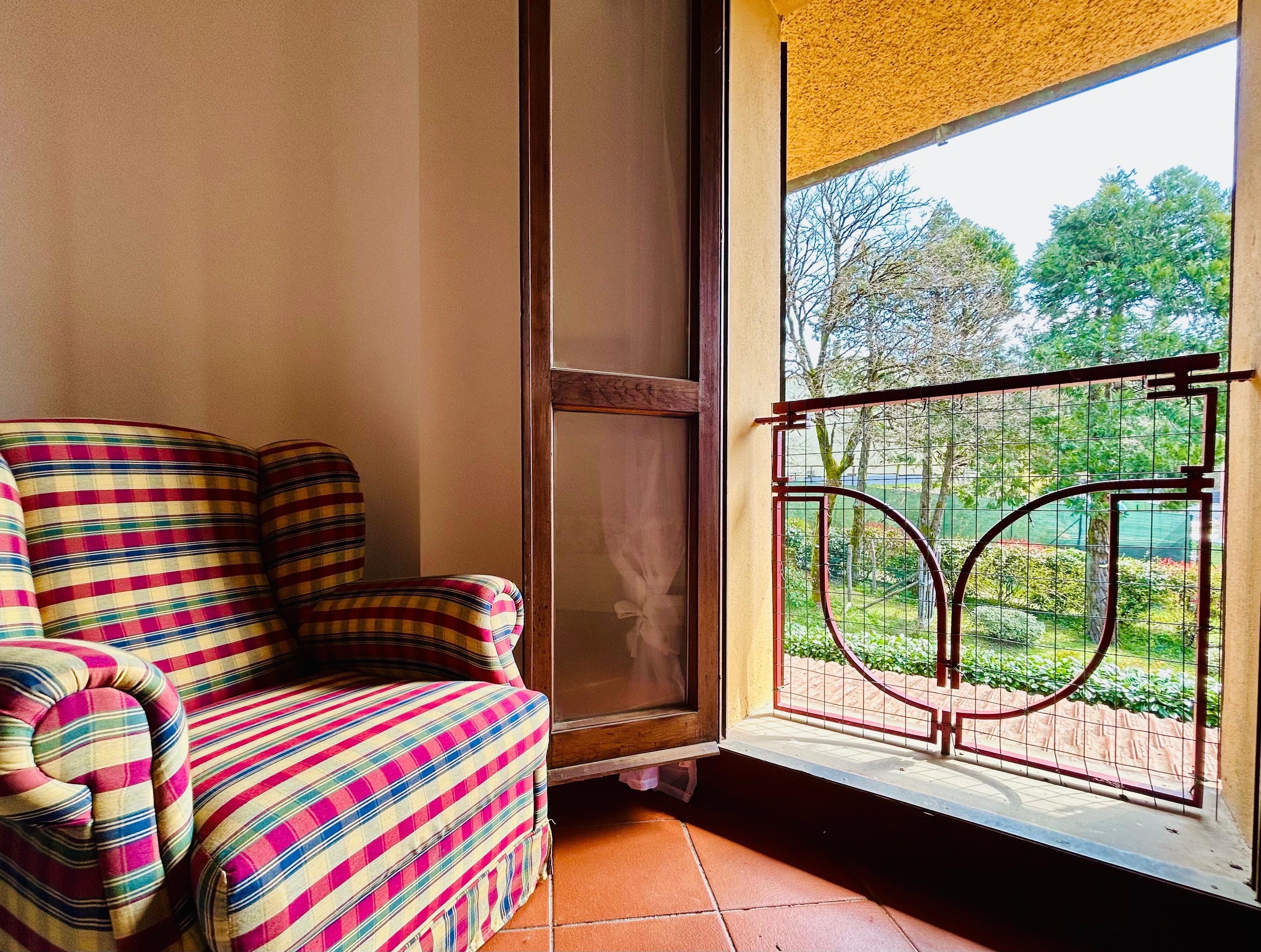 A room with a striped sofa, a window with a metal gate, and a view of greenery outside.
