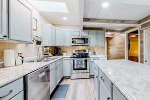 Uma cozinha moderna com armários cinza claro, eletrodomésticos de aço inoxidável e bancada de mármore.