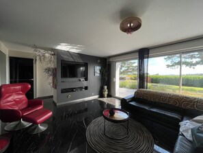 Ein modernes Wohnzimmer mit einem Flachbildfernseher, einem roten Ledersessel, einem schwarzen Sofa und einem großen Fenster mit Aussicht.