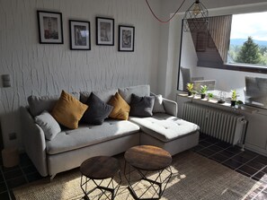 A modern living room with a sofa, two side tables, a radiator, and framed pictures on the wall. - Vacation rental overlooking the lake in Bad Weißenstadt, with a view of the lake-side boarding house  (Weißenstadt)