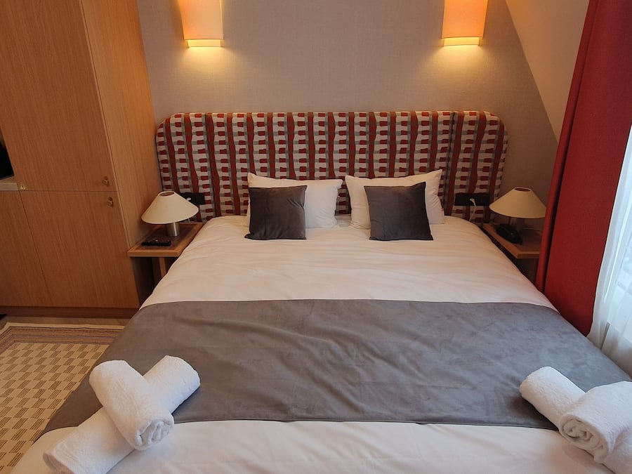 Quarto de hotel com cama, duas mesas de cabeceira, um pequeno kitchenette e uma janela com cortinas.