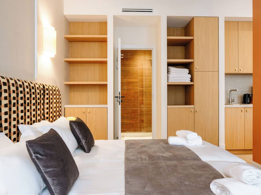 A hotel room with a bed, a wardrobe, a bathroom, and a shower area.
