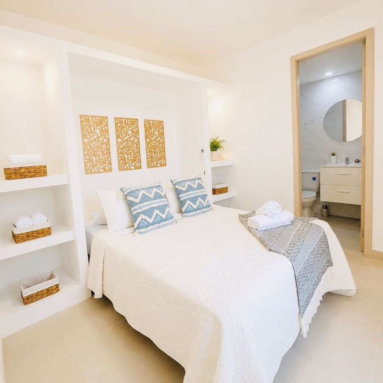 A modern bedroom with a large bed, white walls, and a bathroom visible through an open door.