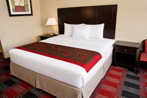 A hotel room with a large bed, a nightstand with a lamp, a chair, and a framed picture on the wall.