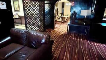 A room with a brown leather sofa, a patterned carpet, a dining area with chairs and a table, and a wall with a decorative panel.