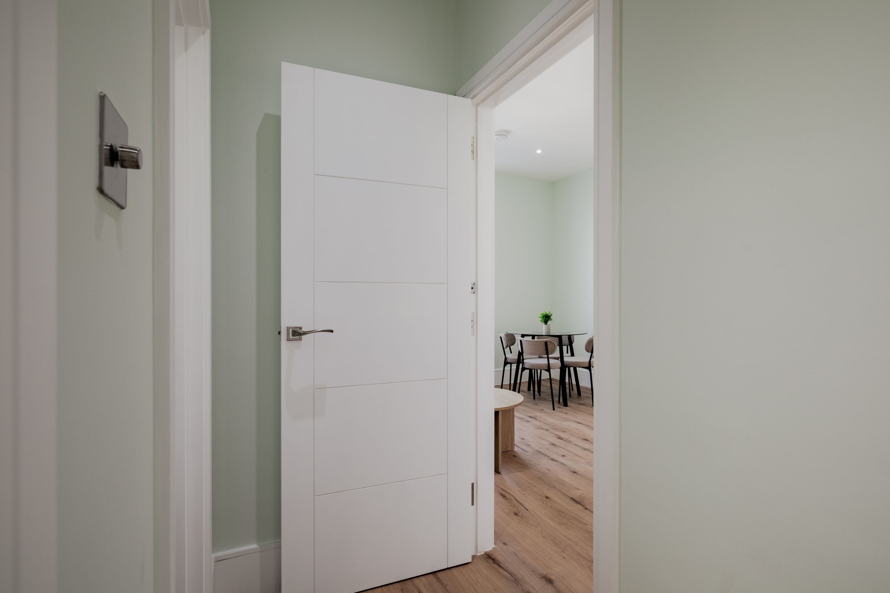 A hallway with a white door leading to a dining area with a table and chairs.
